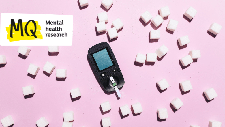 On a pale pink background, white sugar cubes are scattered. At the centre of the image lies an insulin treatment device.